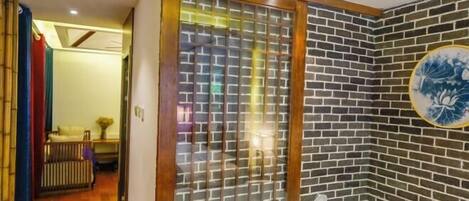 A bathroom with a large bathtub, a wooden-framed glass door, and a brick-patterned wall.