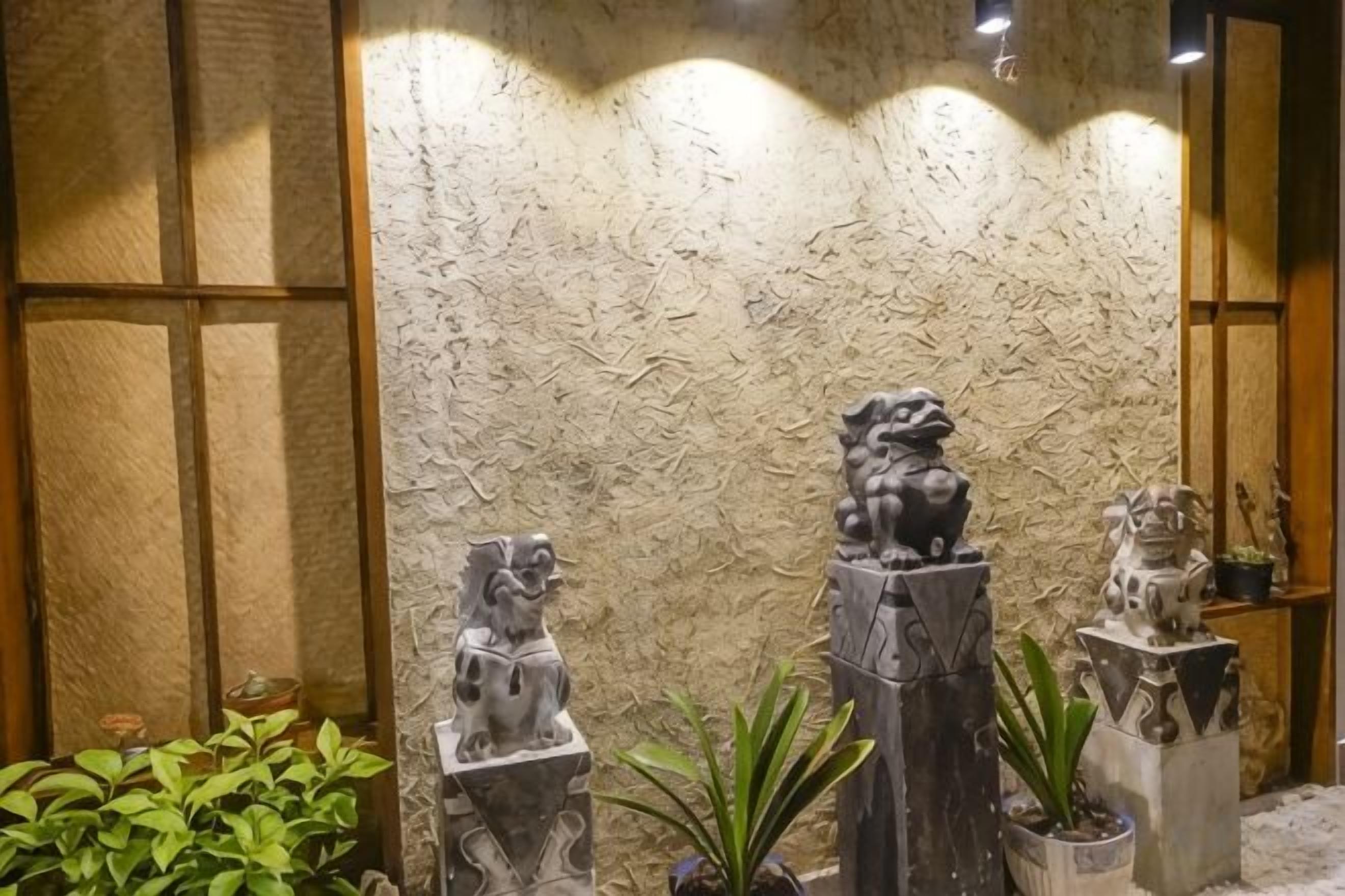 A stone lion statue in a courtyard with a textured wall backdrop.