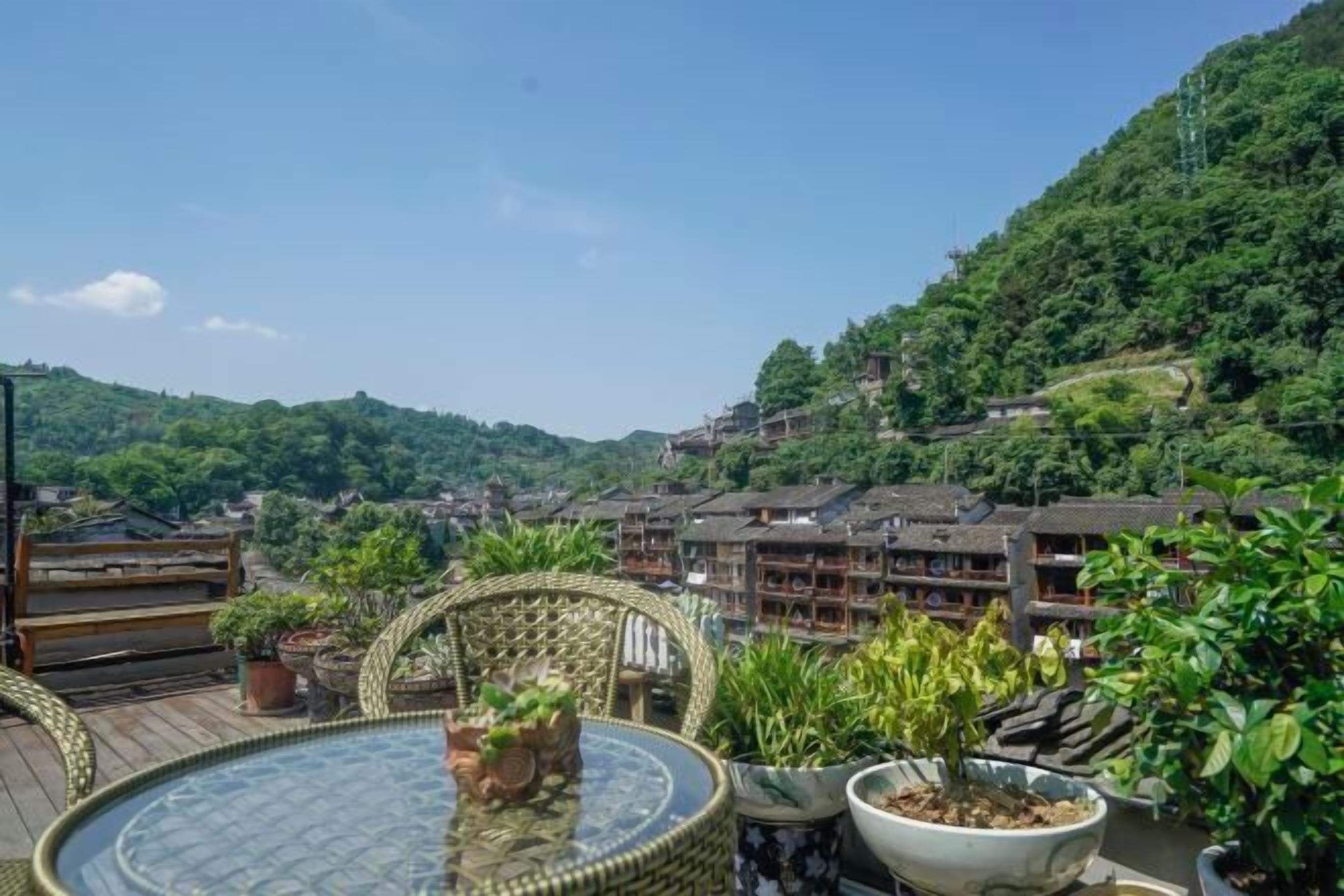 A terrace with wicker furniture and potted plants, overlooking a hillside with traditional buildings.