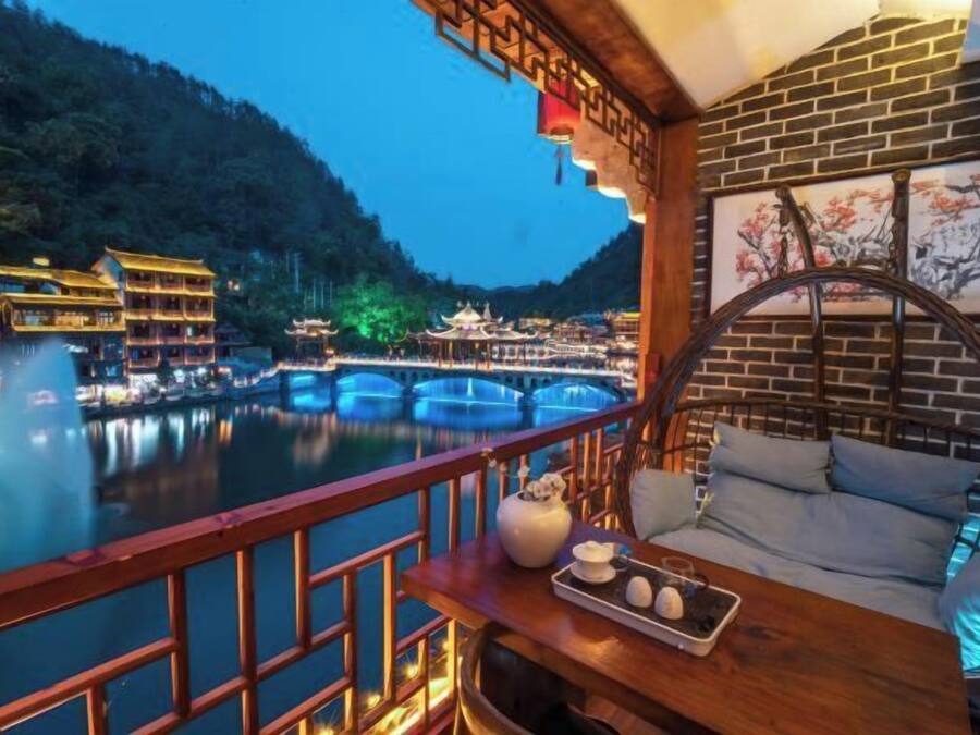 Vista para o rio com edifícios tradicionais, área de refeições com mesa e cadeiras e guarda-corpo de madeira.