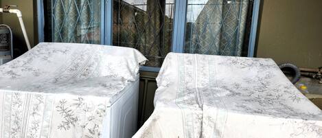 Two beds with floral-patterned covers, a window with metal bars, and a visible water pipe.
