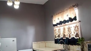 Una cocina con estufa, refrigerador y una ventana con cortinas decorativas.