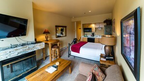 A hotel room with a bed, a TV, a fireplace, a small kitchen area, and a dining table. - Kendall 344: Cozy Studio for 2 in the Heart of Purgatory Resort (Durango)