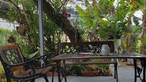 An outdoor seating area with a metal table and bench, surrounded by potted plants and greenery.