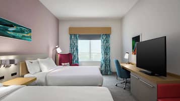 Habitación de hotel con dos camas, un escritorio con televisión, una silla, una lámpara de escritorio y una ventana con cortinas.