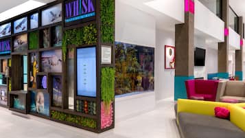 A modern interior with a bar area named WHISK, a digital arrival board, and a seating area with colorful chairs.