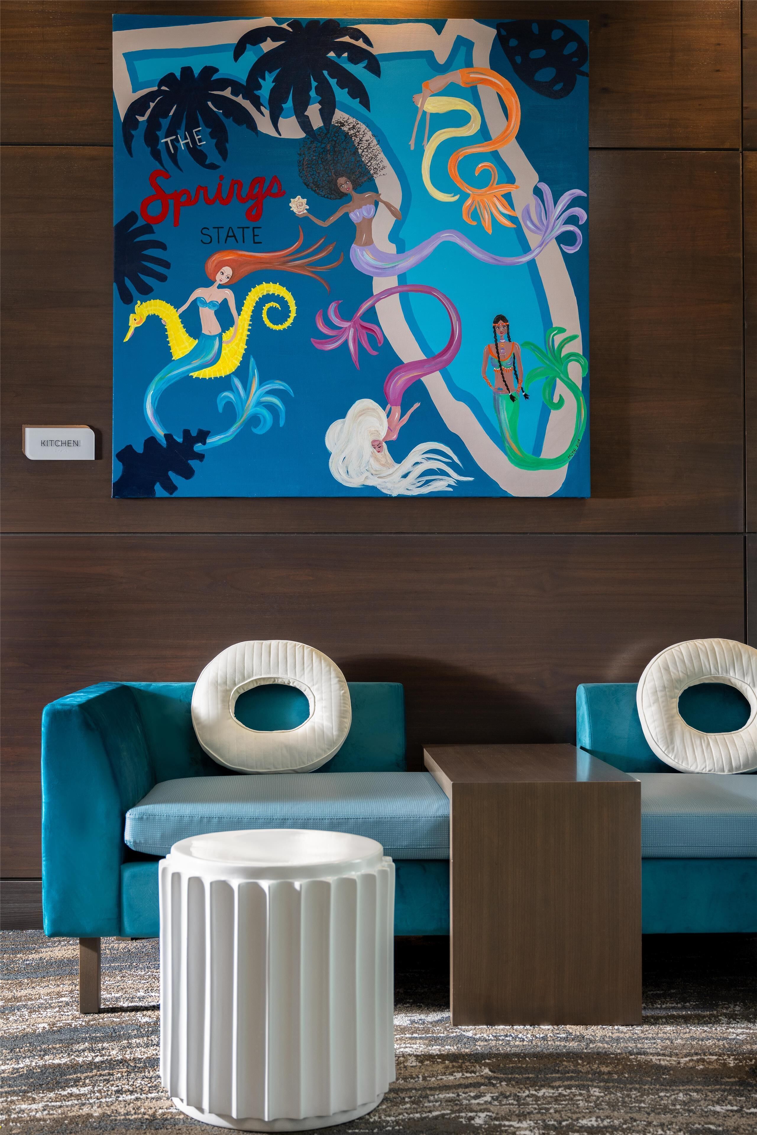 A room with teal sofas, a white ottoman, and a vibrant abstract painting on the wall.
