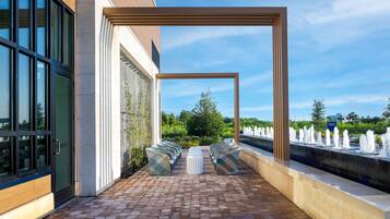 A hotel patio with a brick floor, outdoor seating, a water feature, and a view of the garden.