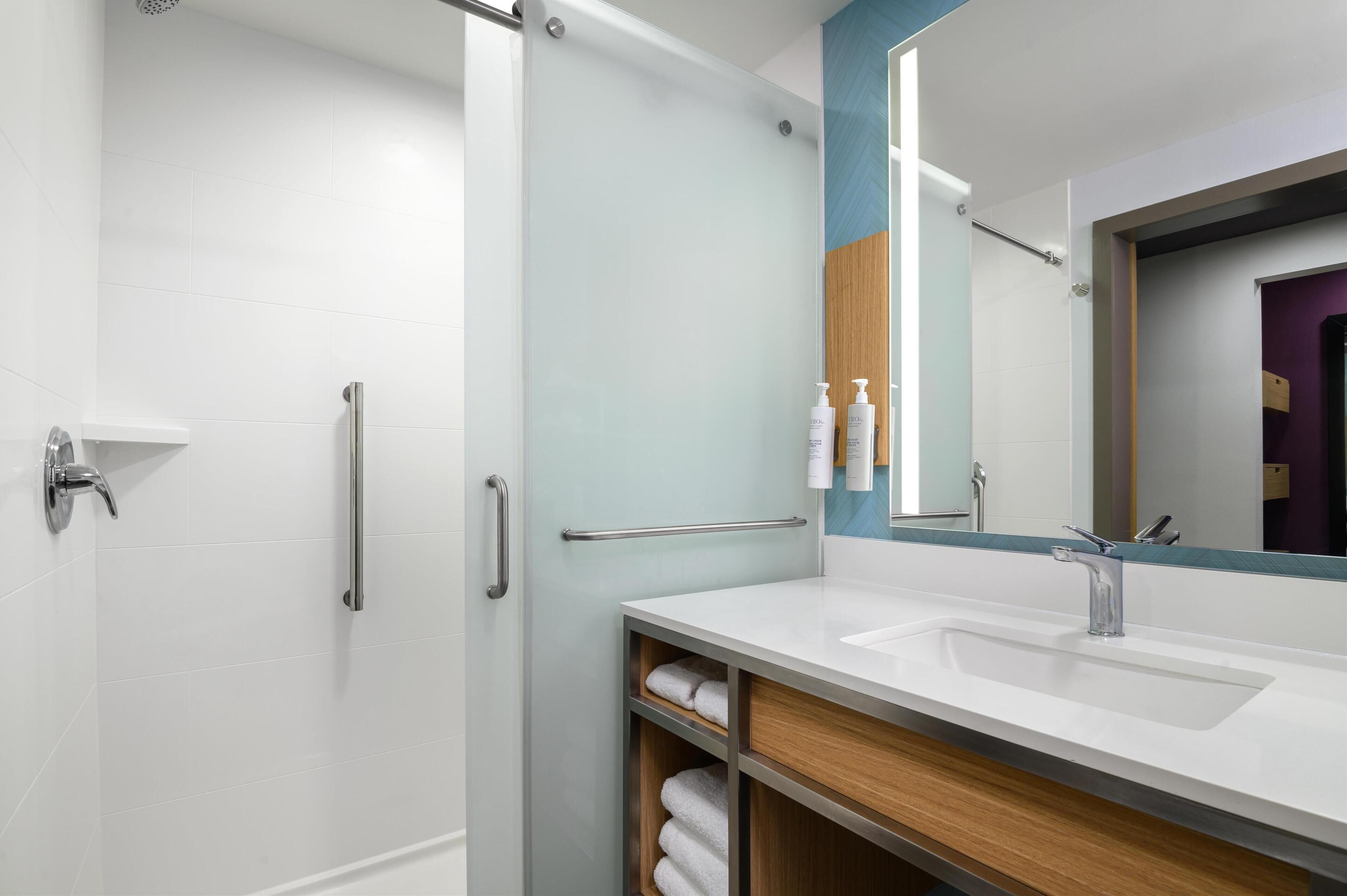 A modern bathroom with a glass shower enclosure, a white sink with a wooden vanity, and a large mirror.