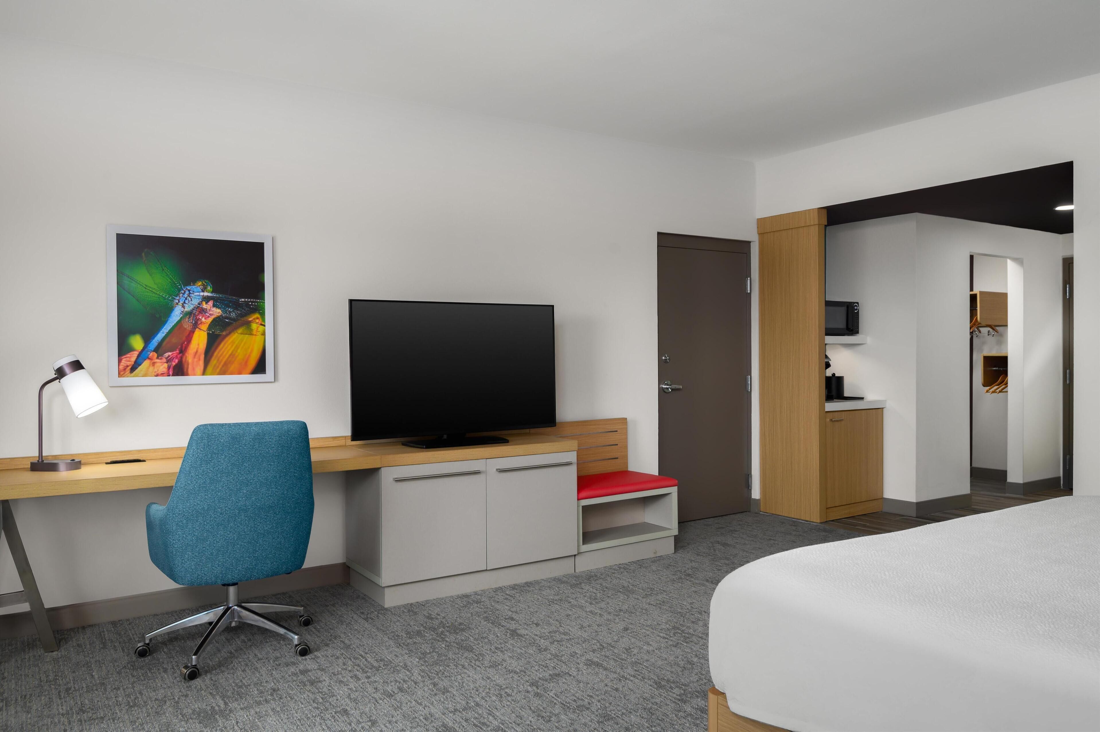 Een hotelkamer met een bureau, stoel, televisie, bed en een kleine kitchenette.