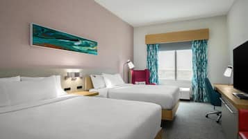 Habitación de hotel con dos camas, un escritorio, un televisor, una ventana con cortinas y un cuadro en la pared.