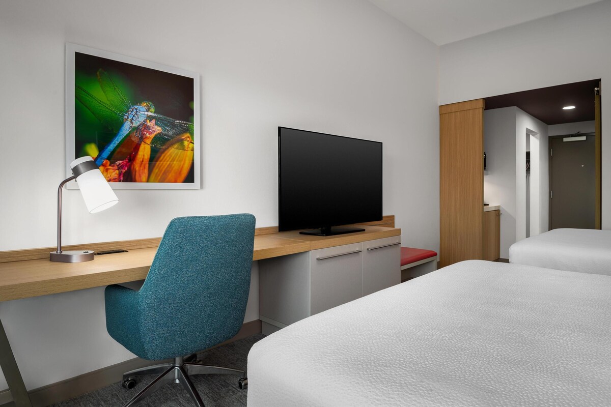 A hotel room with a desk, a television, a chair, a bed, and a door leading to another room.