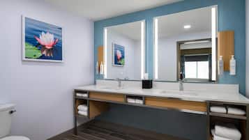 A modern bathroom with a large mirror, two sinks, and a toilet. There are towels and toiletries on the counter.