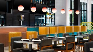Un restaurante moderno con una zona de bar, asientos con cabinas tapizadas en amarillo y negro, e iluminación colgante.