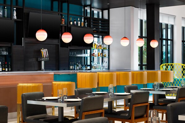 Ein modernes Restaurant mit Bar, Sitzgelegenheiten mit gelb-schwarzen Polsterbänken und Pendelleuchten.
