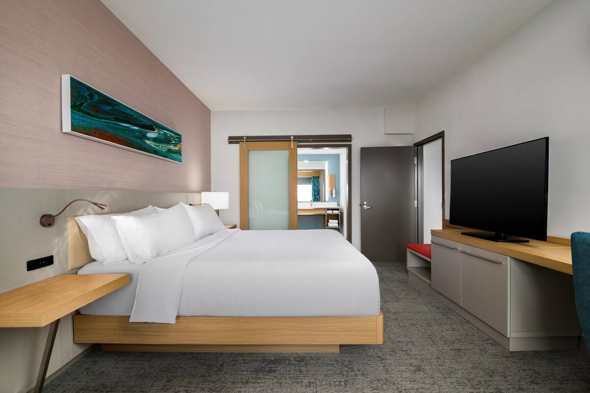 Ein modernes Hotelzimmer mit Bett, Nachttisch, Fernseher und einem Gemälde an der Wand.