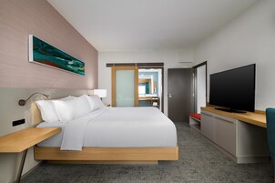 Une chambre d’hôtel moderne, équipée d’un lit, d’une table de chevet, d’une télévision et ornée d’un tableau au mur.