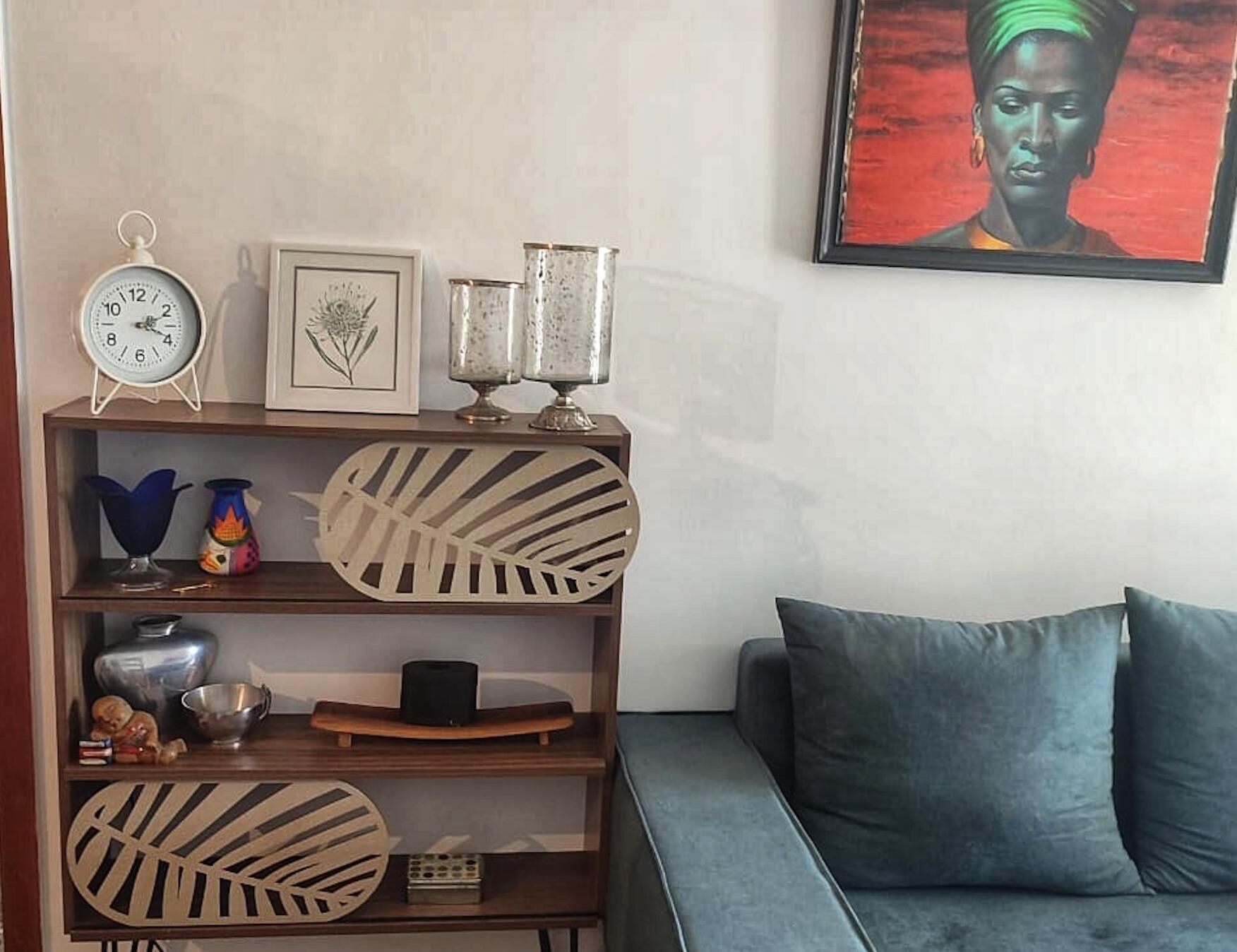 A living room with a blue sofa, a wooden side table with decorative items, a clock, and a framed picture on the wall.