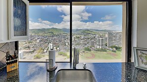 Eine Küche mit einem großen Fenster und Blick auf die Stadt, einem Spülbecken und einer Arbeitsfläche mit Messerblock.