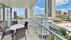 A balcony with a round table and chairs, overlooking a cityscape with tall buildings and a clear sky. - Pacific Monarch Paradise 1-Bedroom | Ocean Views (Honolulu)