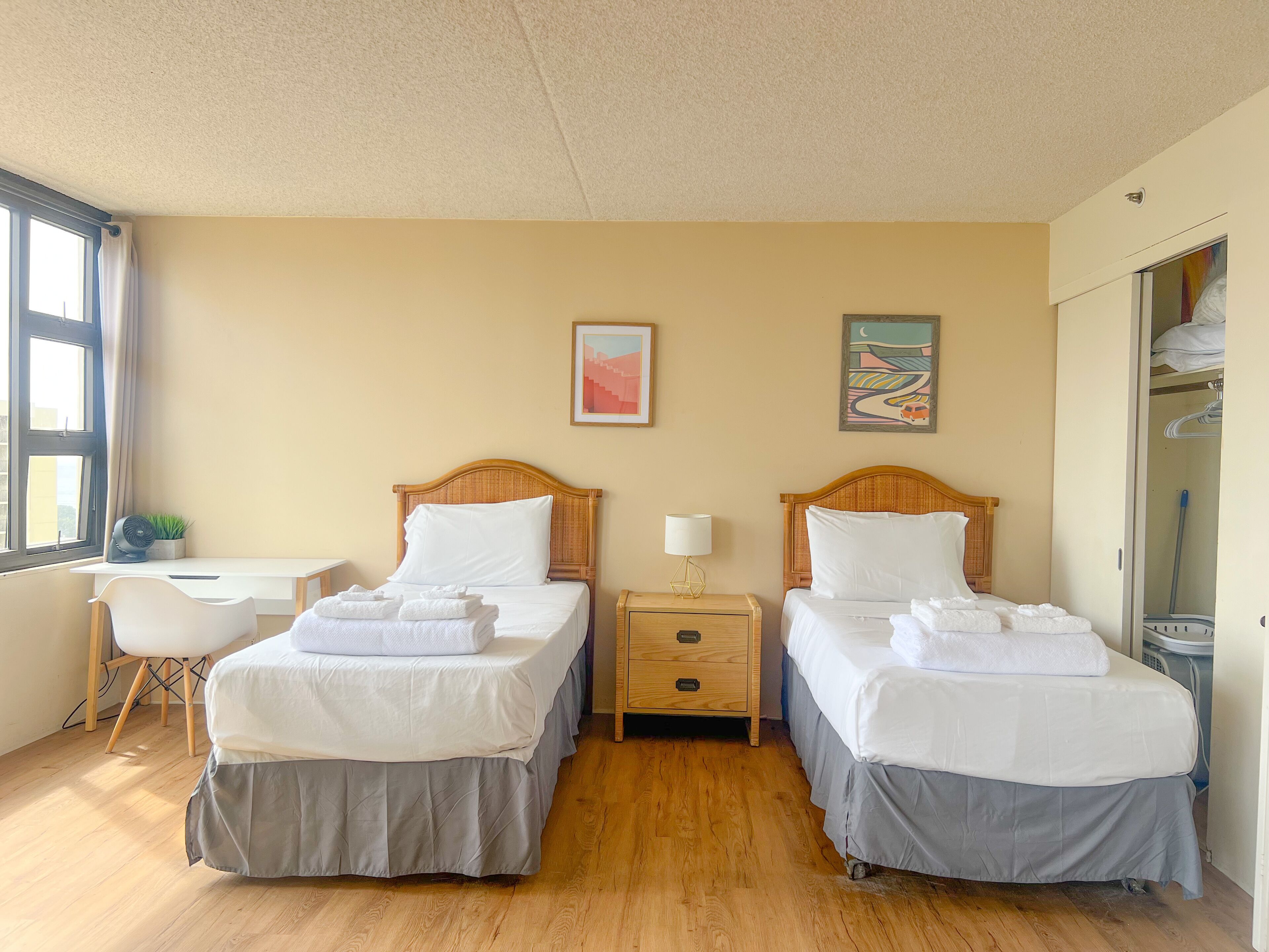 A hotel room with two single beds, a desk, a chair, and a wardrobe.