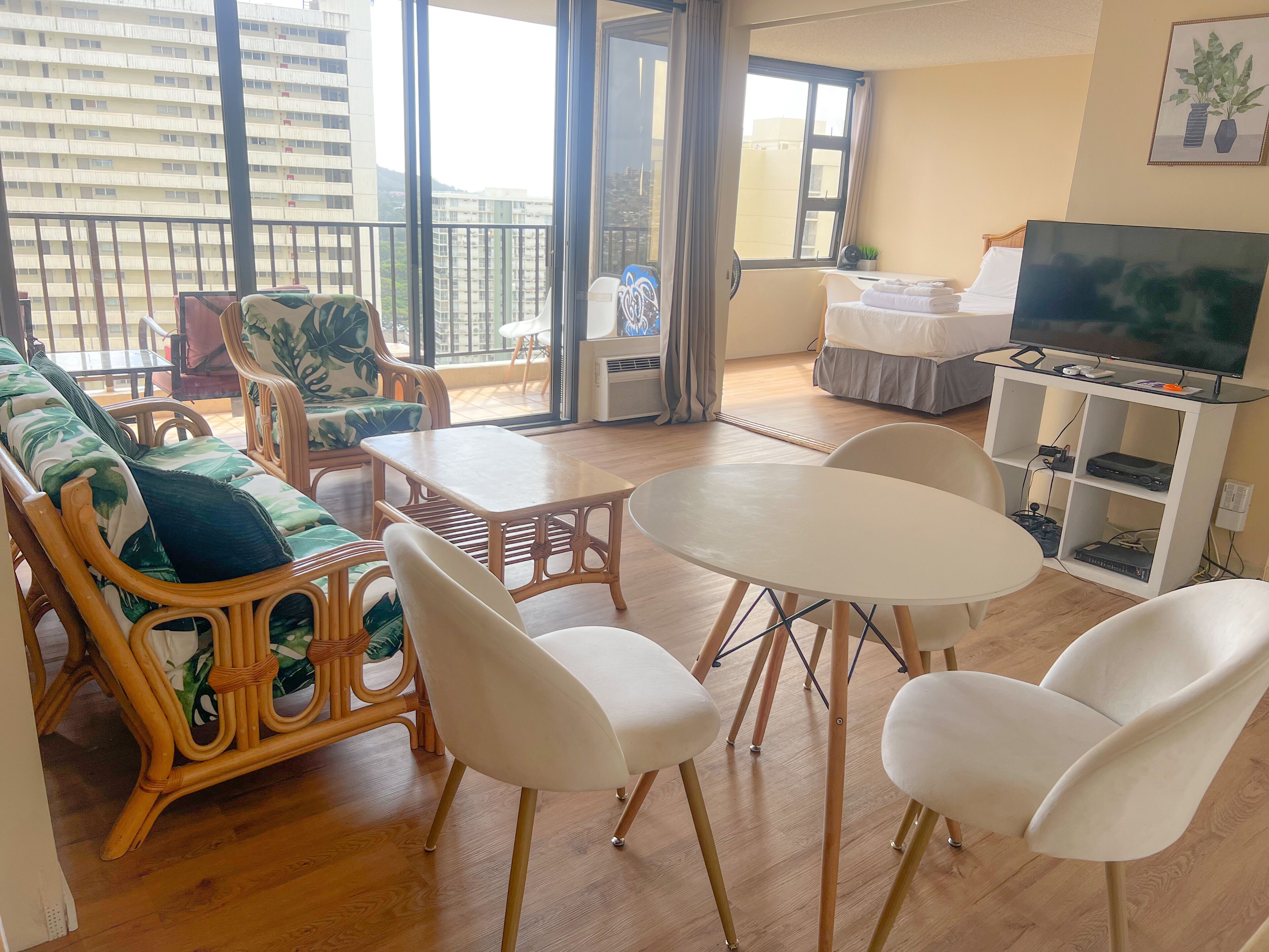A living room with a sofa, chairs, a table, a TV, and a balcony with a view of buildings.