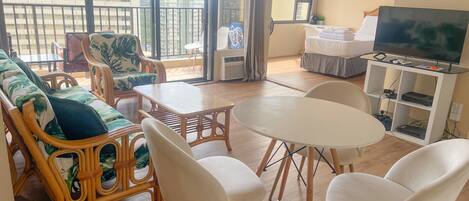 A living room with a sofa, chairs, a table, a TV, and a balcony with a view of buildings.