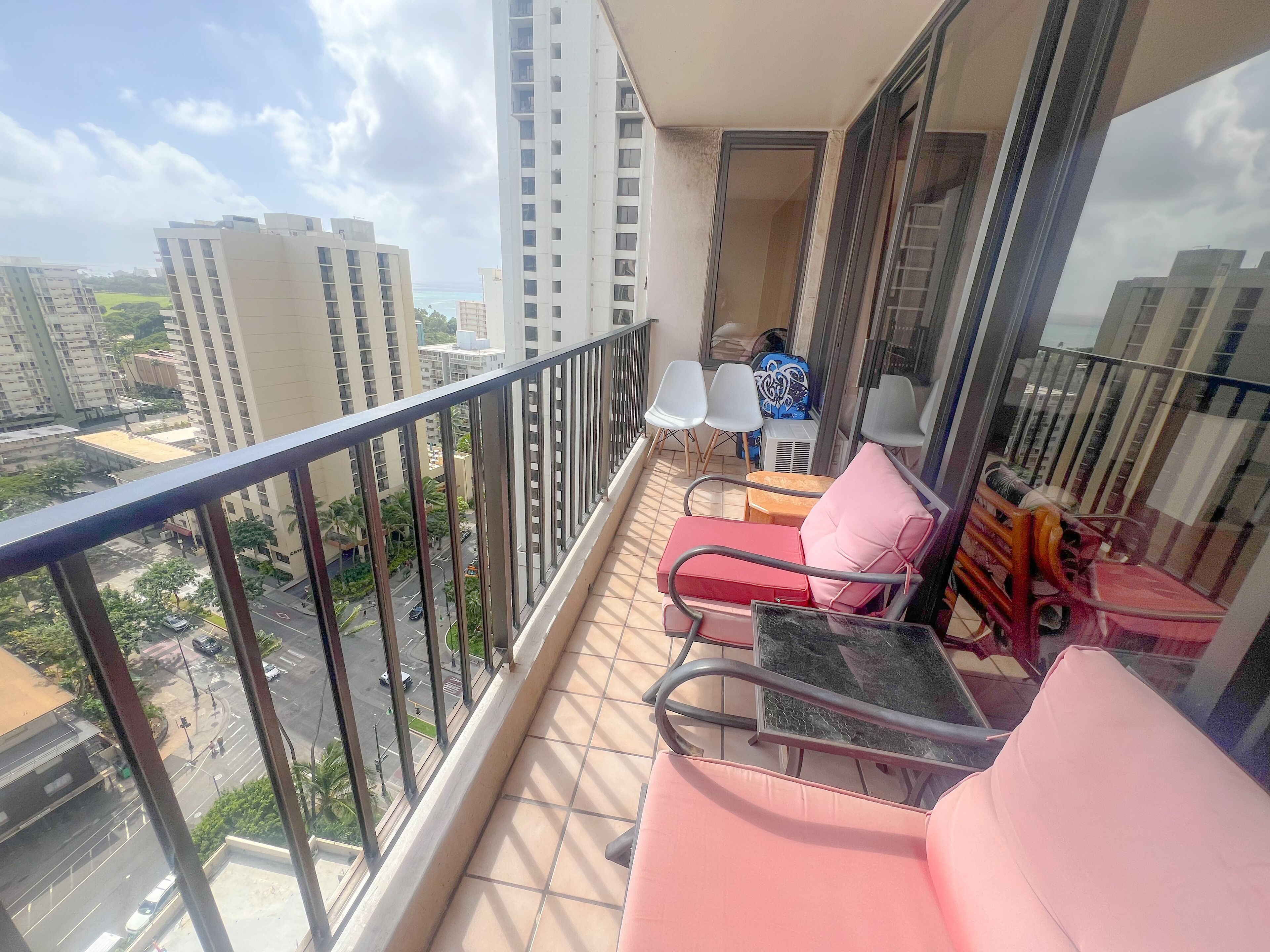 A balcony with a glass railing, a small table, two chairs, and a sofa.