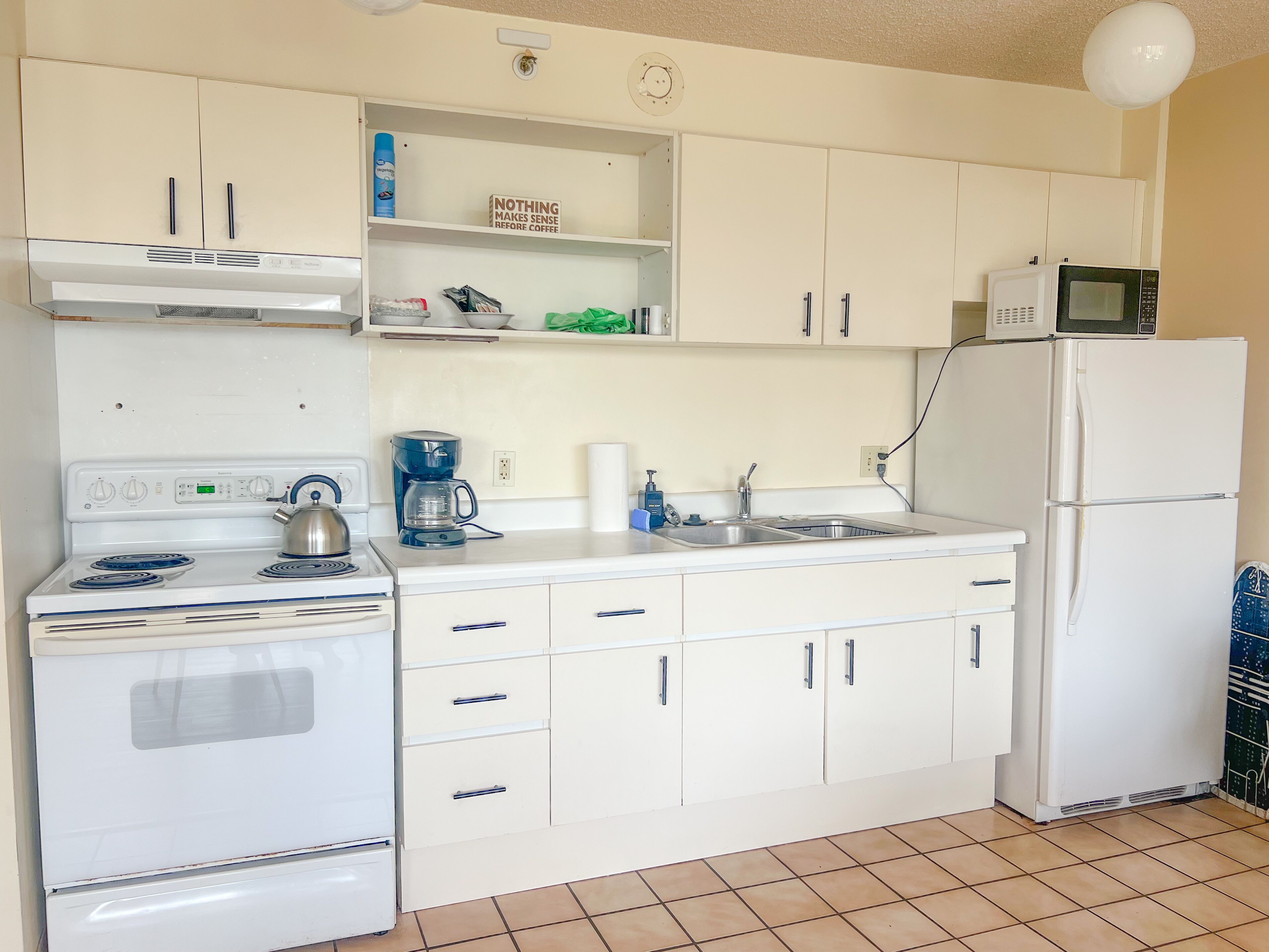 A compact kitchen with white cabinets, a stove, a microwave, and a sink.