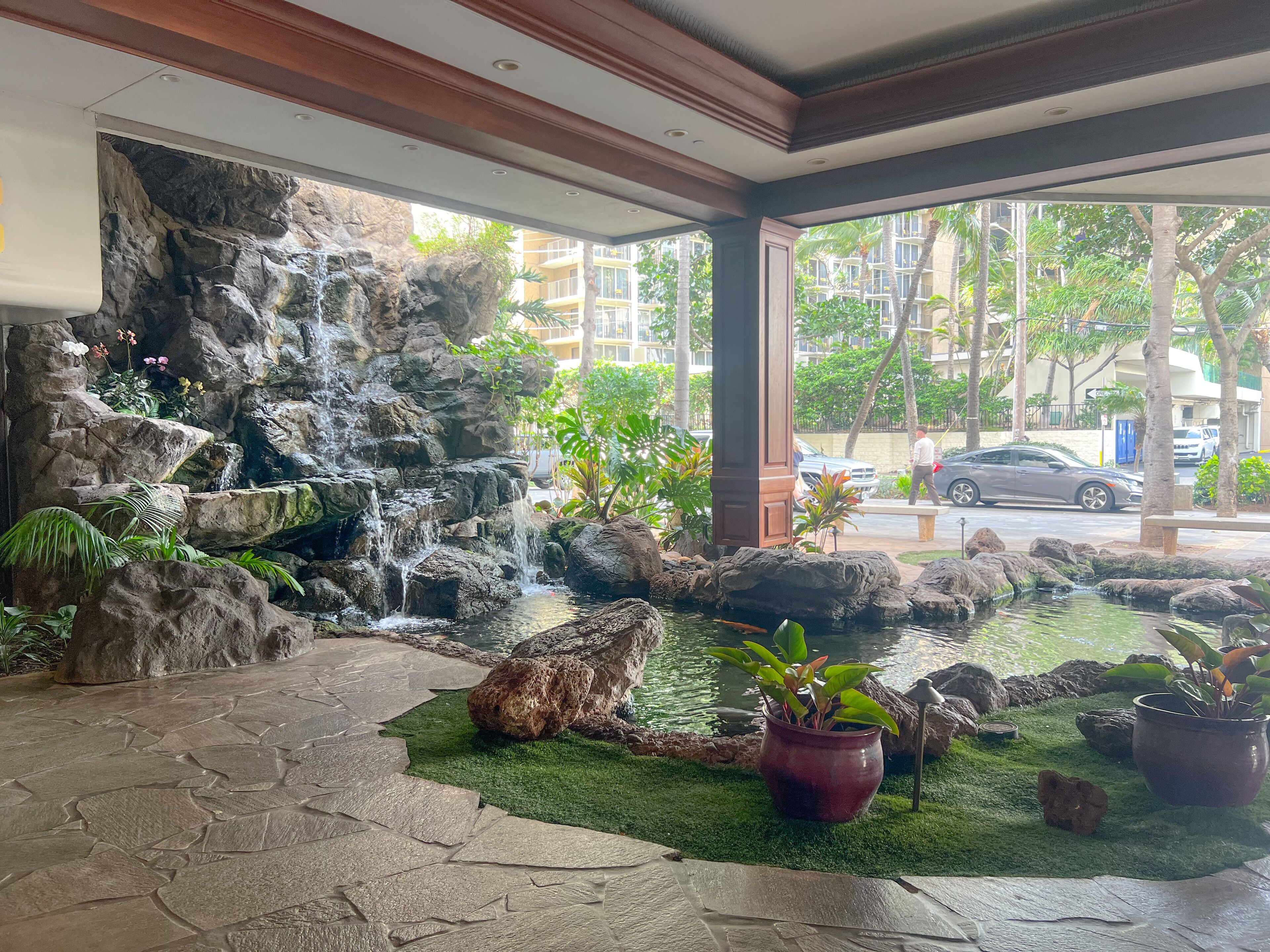 Un vestíbulo de hotel con una cascada, suelo de piedra y plantas en macetas.