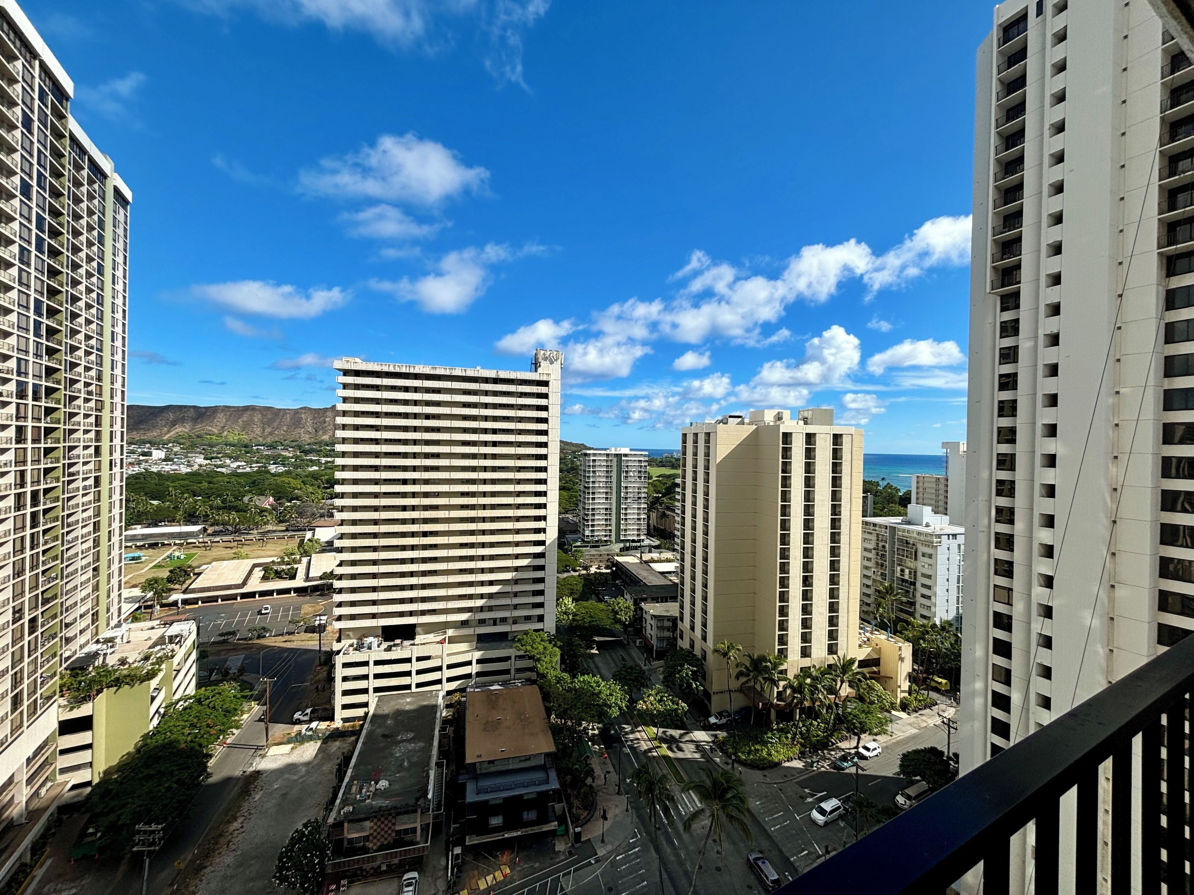 A high-rise building with a flat roof and multiple balconies, surrounded by other buildings and a clear sky.