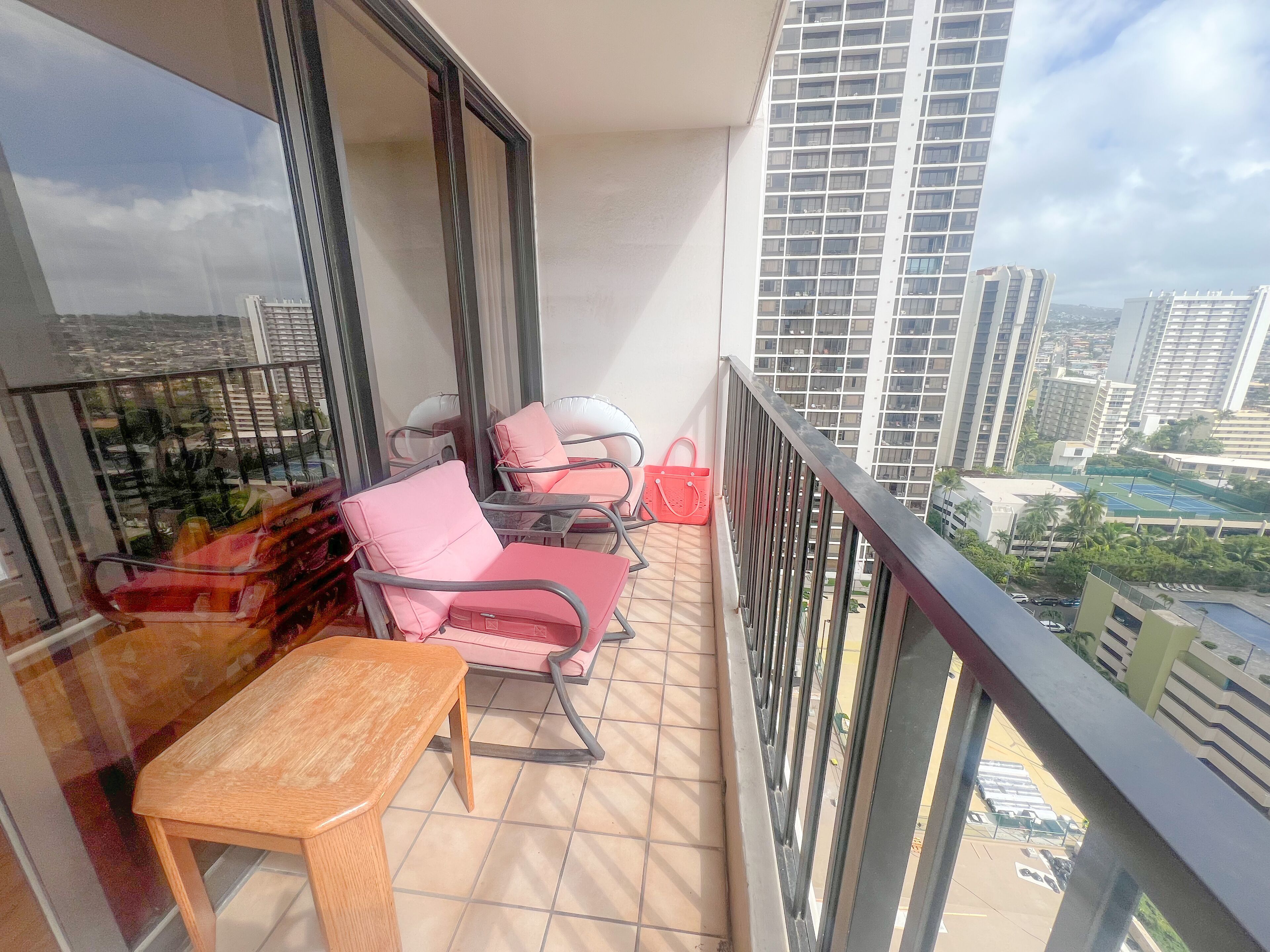 Ein Balkon mit zwei Stühlen und einem Tisch, der auf einen Stadtblick mit hohen Gebäuden blickt.
