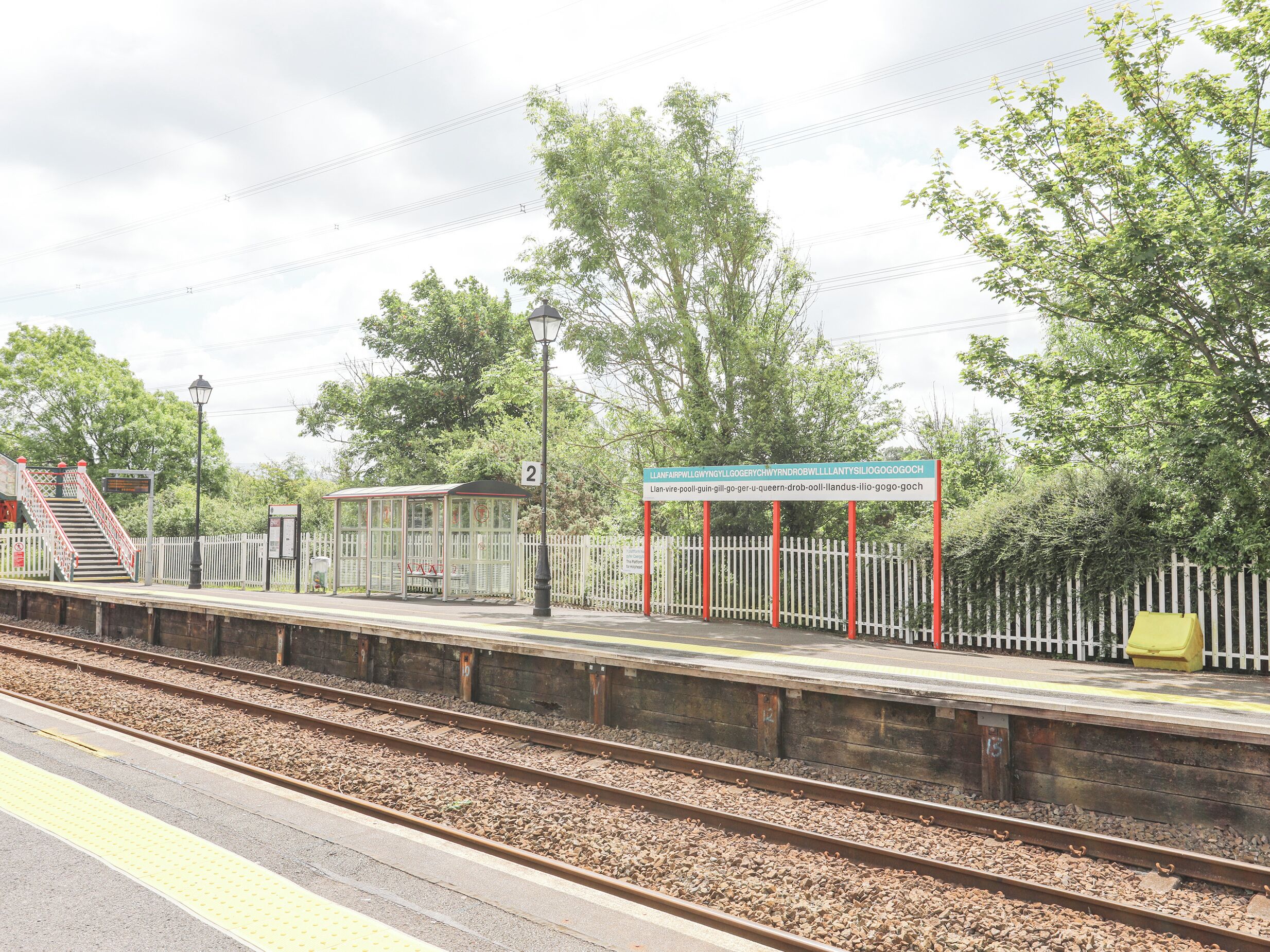 A train station platform with a shelter, a sign, and a fence.