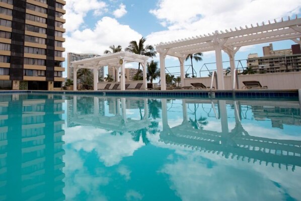 A swimming pool with a clear reflection, surrounded by white pergolas and lounge chairs.
