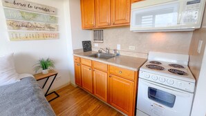 A compact kitchen with wooden cabinets, a white stove, and a microwave. - Bright Hawaiian Monarch Studio | Full Kitchen (Honolulu)