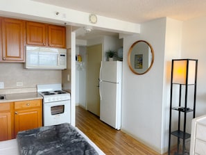 A compact kitchen with wooden cabinets, a microwave, a stove, and a refrigerator.