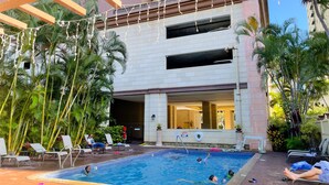 Un espace piscine aménagé avec des chaises longues, une piscine et des palmiers.