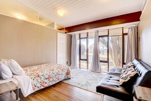 Relax in a spacious bedroom with a large bed, a comfortable sofa, and a window offering a view of the surrounding trees.