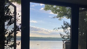 Ett rum med ett stort fönster med utsikt över en vattenyta, en krukväxt och ett litet bord med en flaska på.
