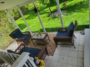 Une terrasse extérieure aménagée avec des meubles en osier, une table en verre et une vue sur une pelouse bien entretenue.