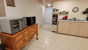 Keittiössä on puinen kaappi, mikroaaltouuni ja pieni uuni. Työtasolla on pesuallas, jonka yläpuolella on kello, sekä kasvi.