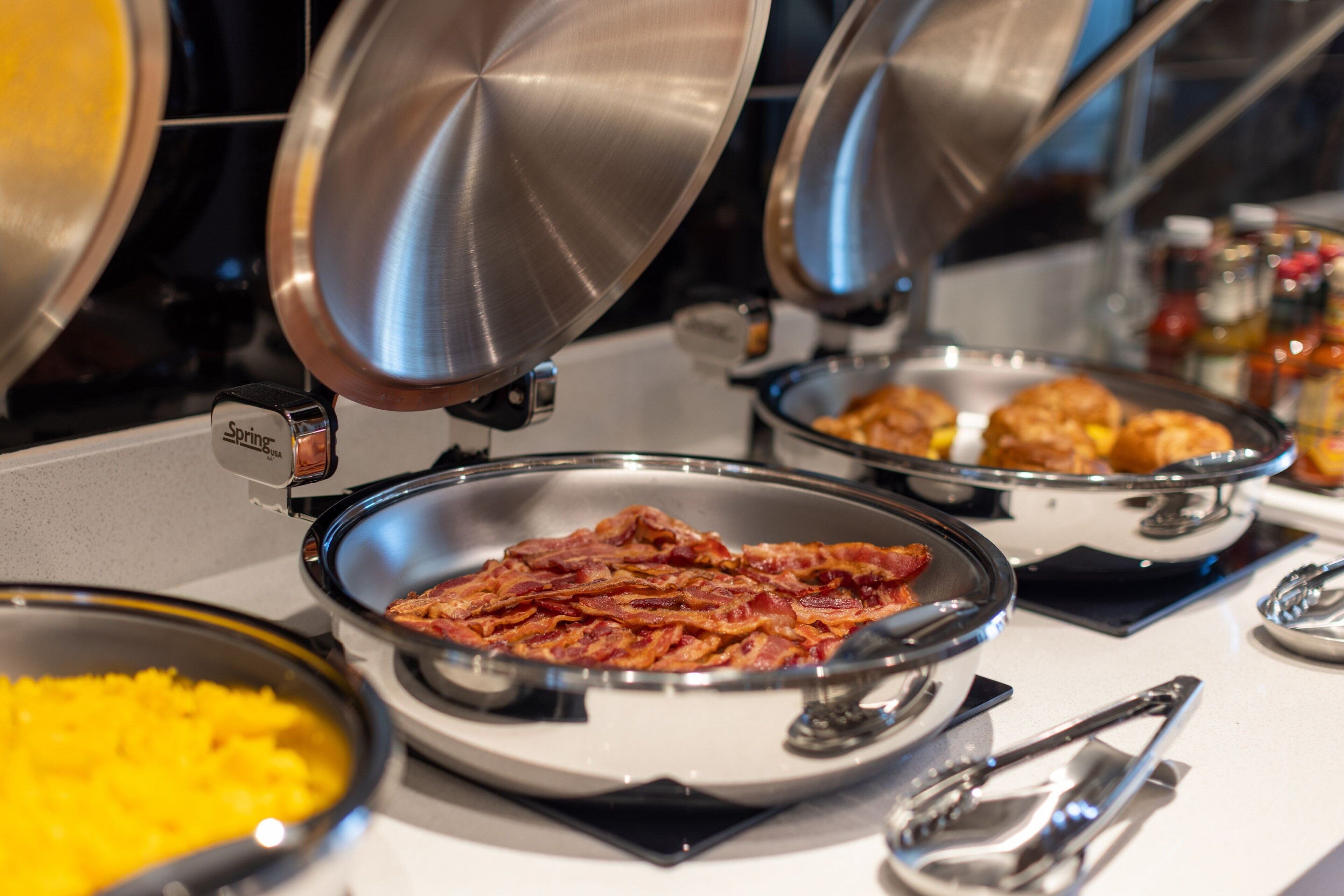A buffet with various food items, including bacon and scrambled eggs, served in metal bowls.