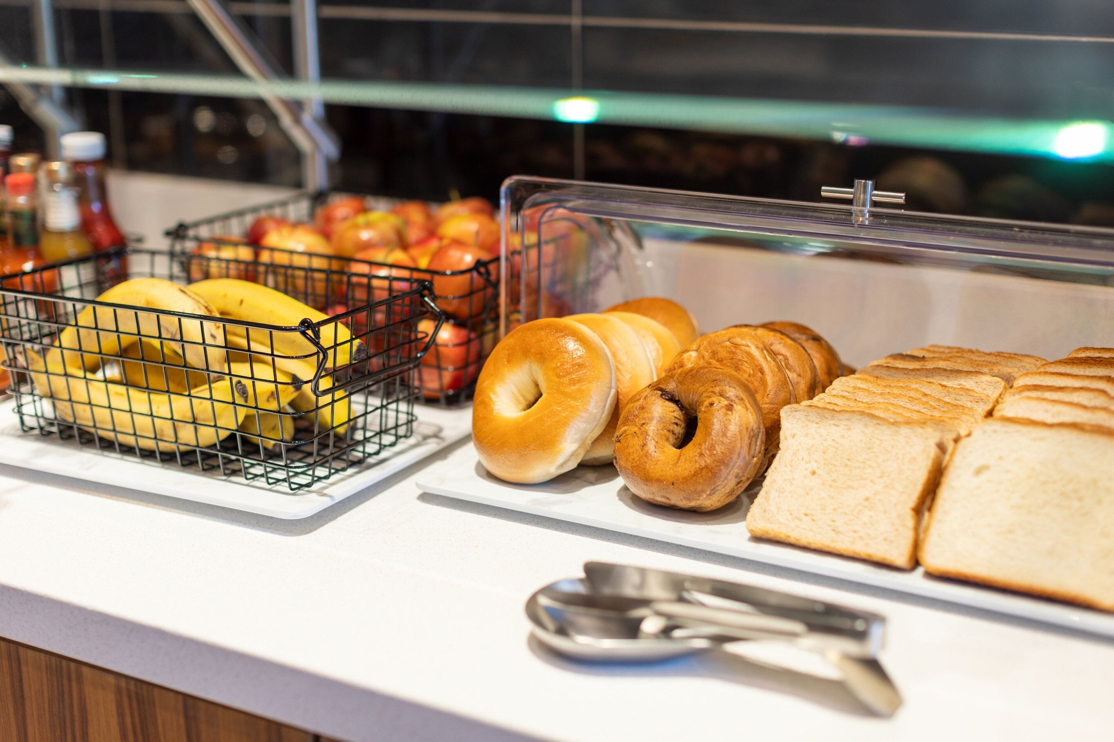 A breakfast buffet with bananas, apples, bagels, and bread.