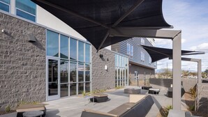 An outdoor patio area with modern seating, a stone wall, and large windows. - SpringHill Suites Tucson at The Bridges (Tucson)