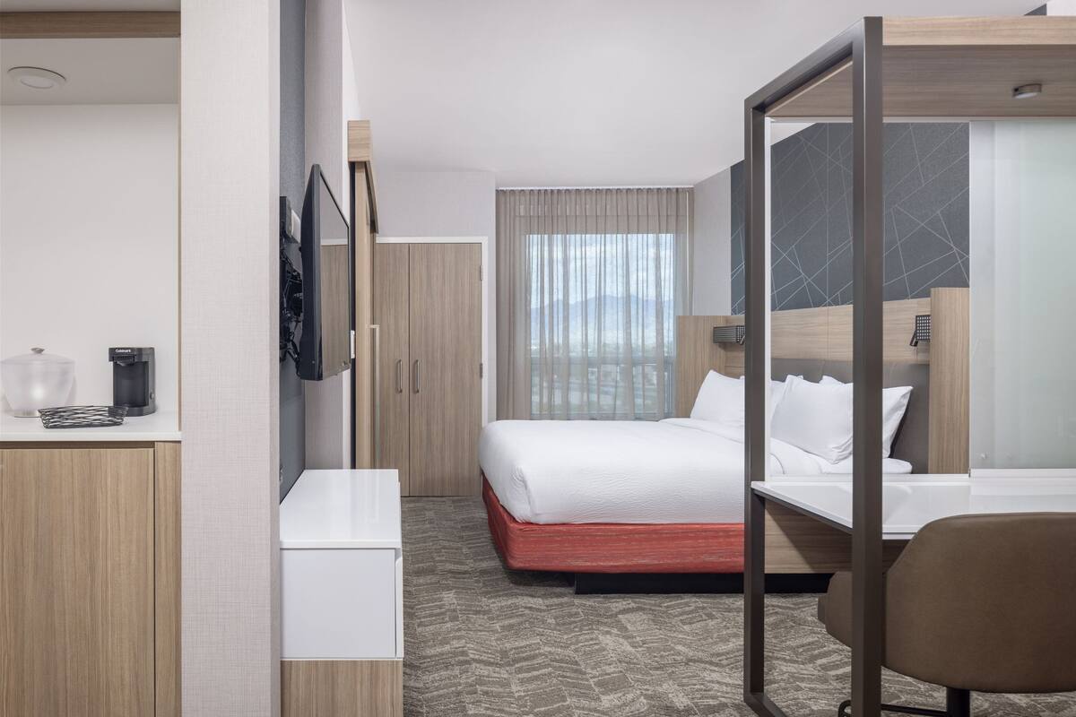A hotel room with a bed, a desk, a chair, a TV, and a window with curtains.