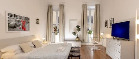 A modern bedroom with a bed, bedside tables, a TV, and a desk.