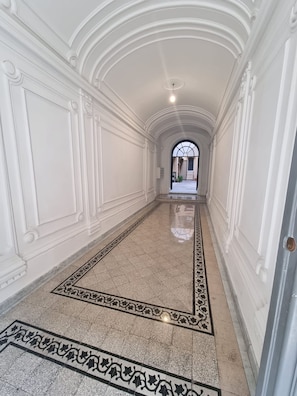 A hallway with white walls, a marble floor, and a patterned rug.