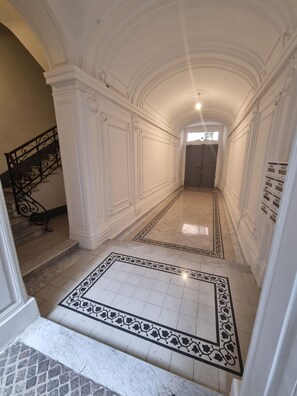 Um corredor com paredes brancas, chão de azulejos e um tapete com padrão preto e branco.