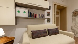 A room with a sofa, a wooden side table, a bookshelf, and a wall clock. - Babuino Deluxe - Spanish Steps (Rome)