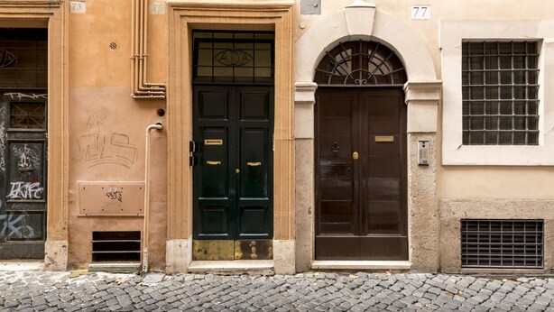 A building facade with two doors, one with a glass panel and the other with a metal grille. - Saint Caterina House - Campo de Fiori (Rome)